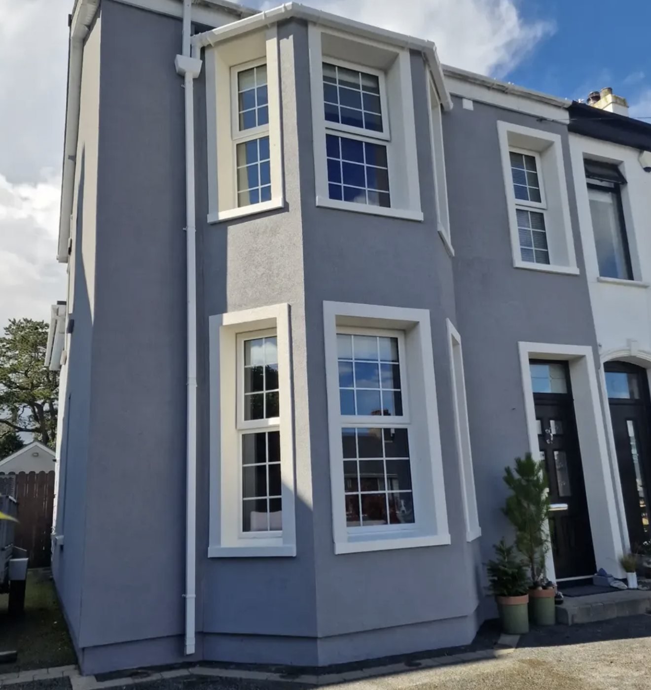 End-of-terrace house in grey textured render with white window surrounds and a two-storey bay