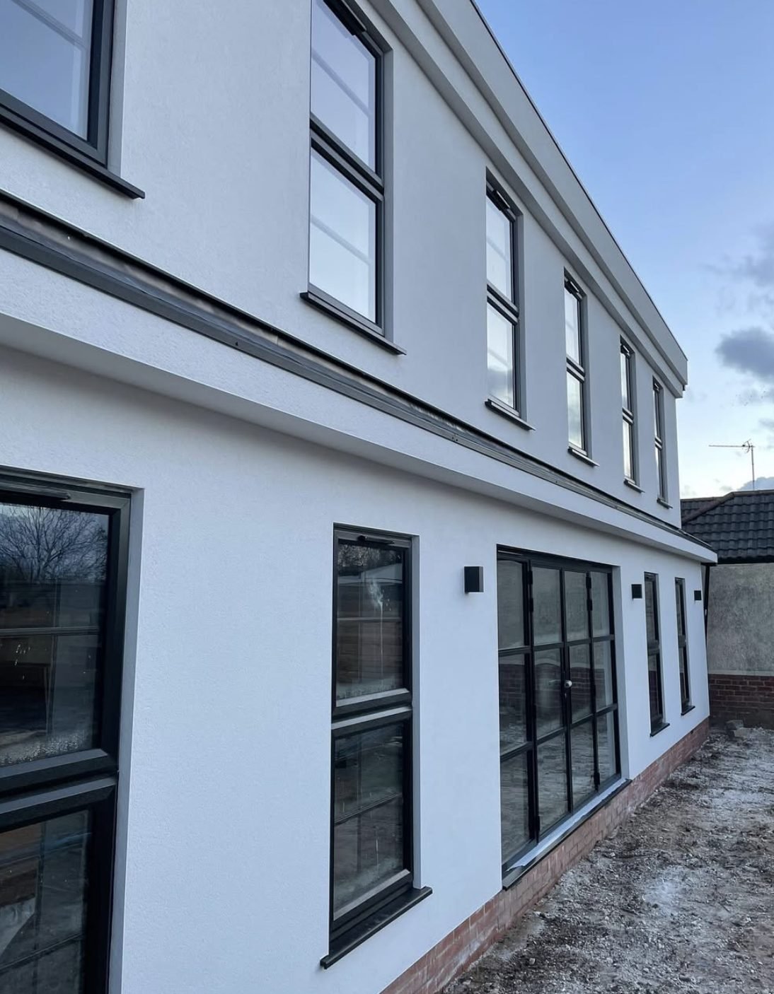 Long flank wall in white with a dark band course and black windows