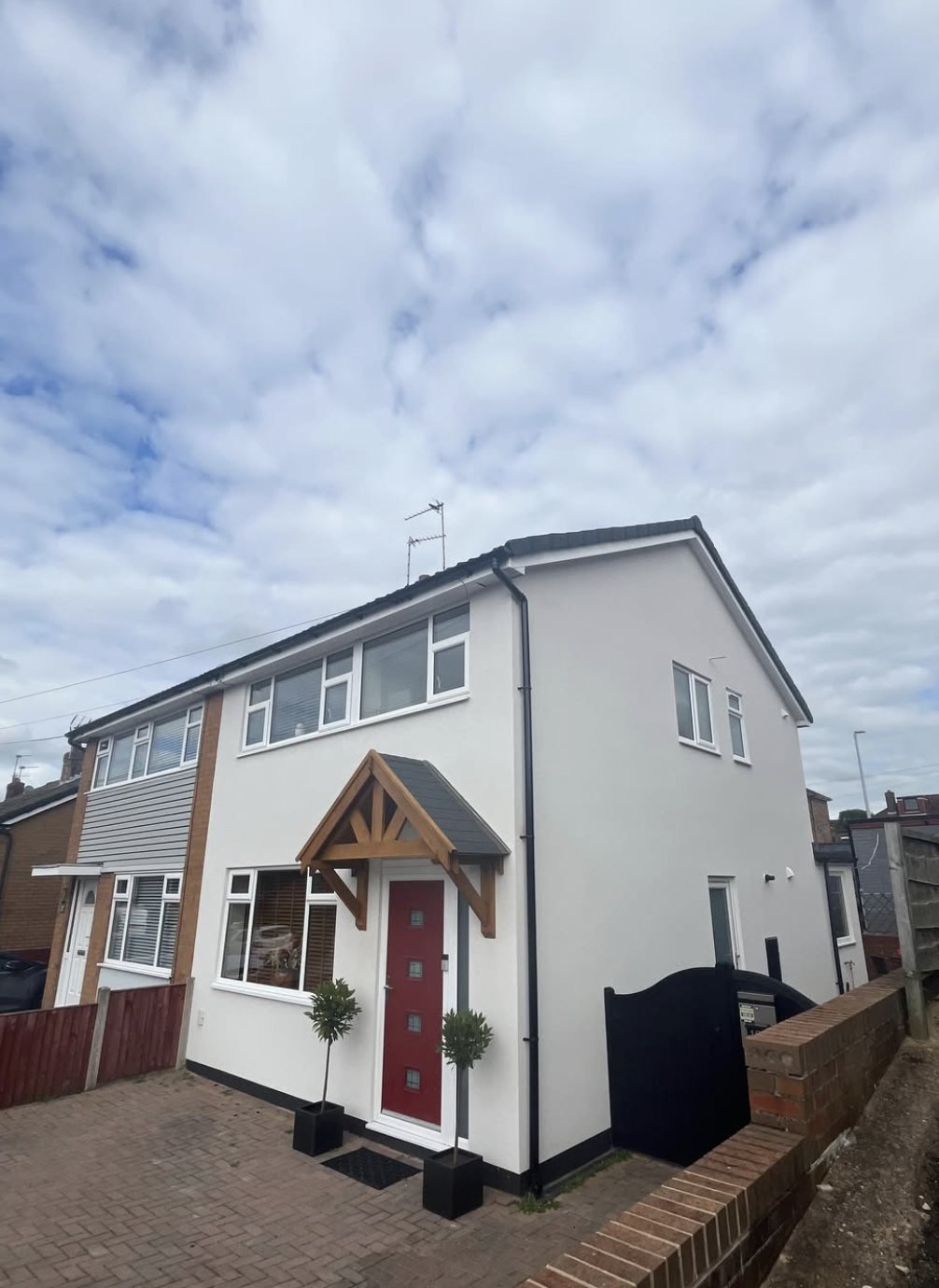 Semi-detached house in white with a dark plinth, oak canopy and red front door