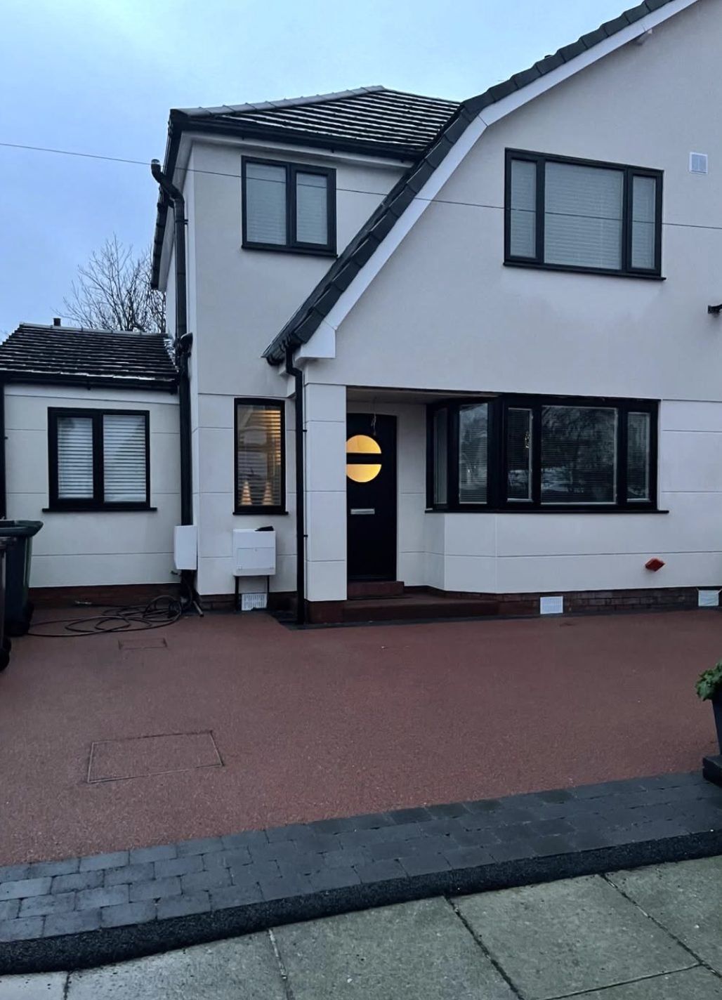 House in white with anthracite window frames and a red paved drive